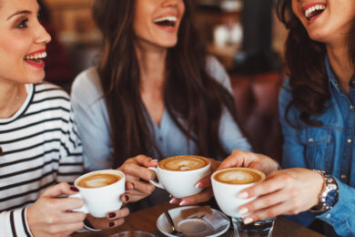 Drie dames die energie krijgen van het drinken van een kop koffie. Maar wat is gezonder, koffie of energiedrank?