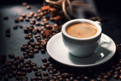 Kopje dampende espresso met op de achtergrond koffiebonen