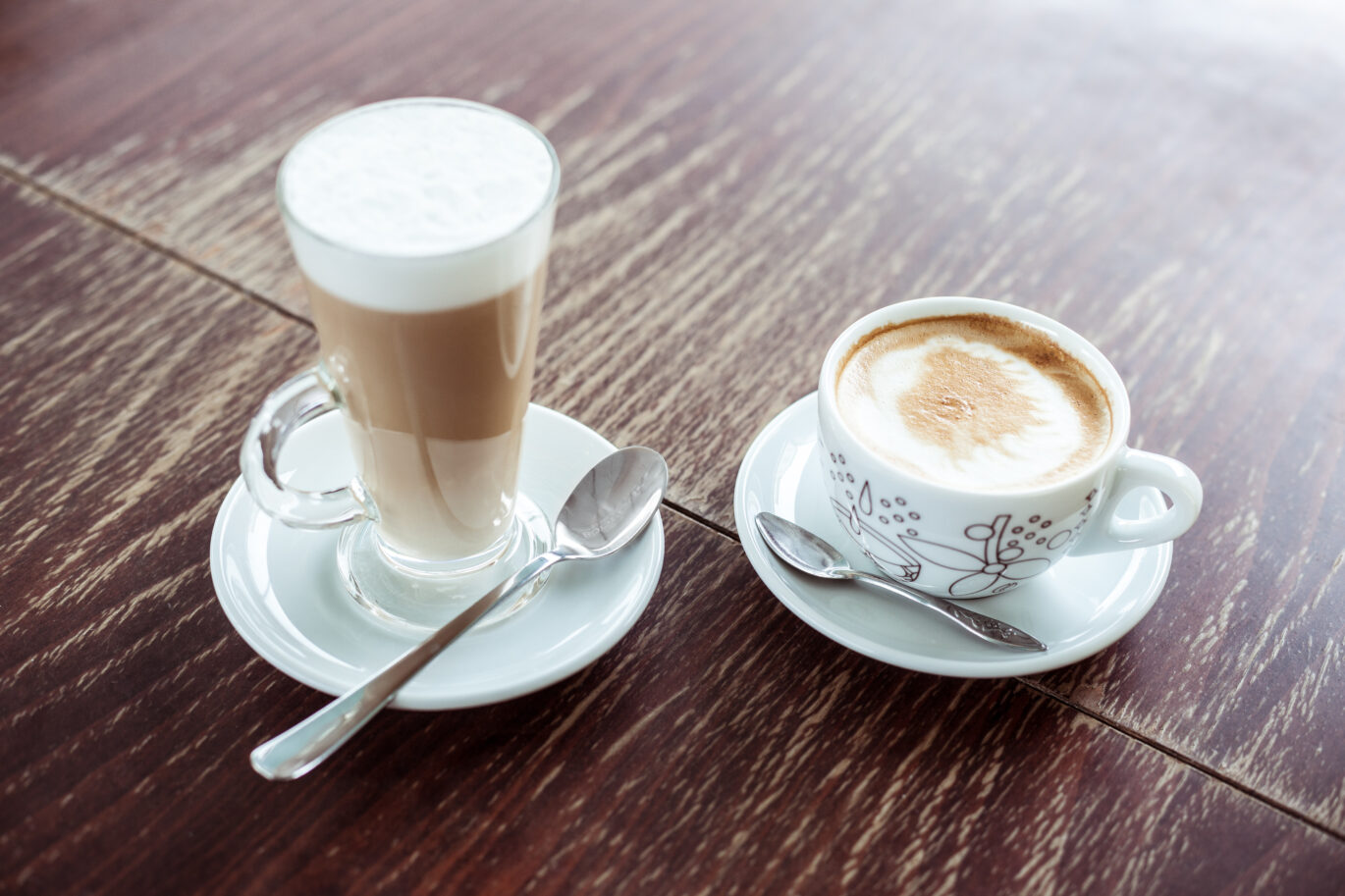 Kopje latte macchiato en een kopje cappuccino op een houten tafel. Maar wat is het verschil tussen latte macchiato en cappuccino?